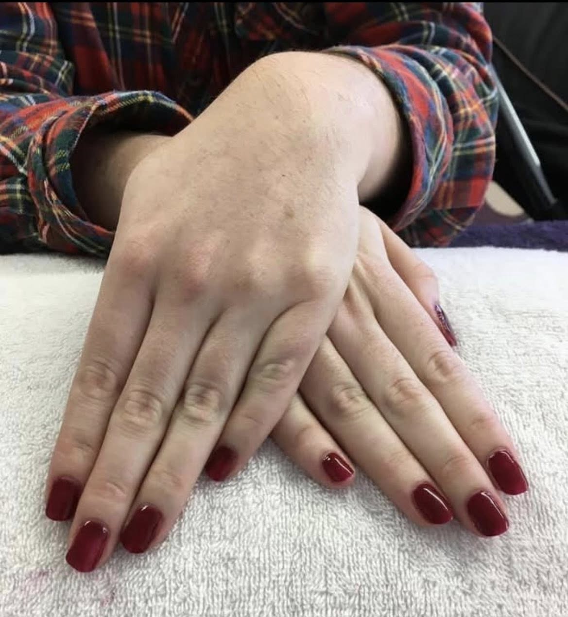 Wine red gel manicure framed by a tartan shirt cuff on a white towel.