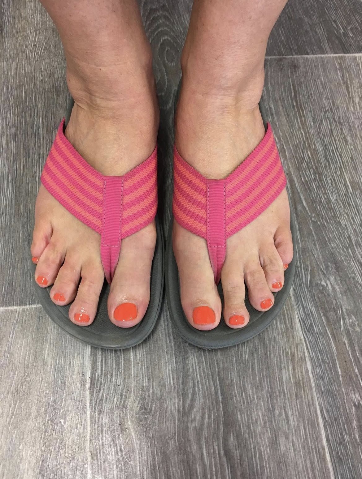 Coral orange pedicure worn with pink and coral striped flip-flops.