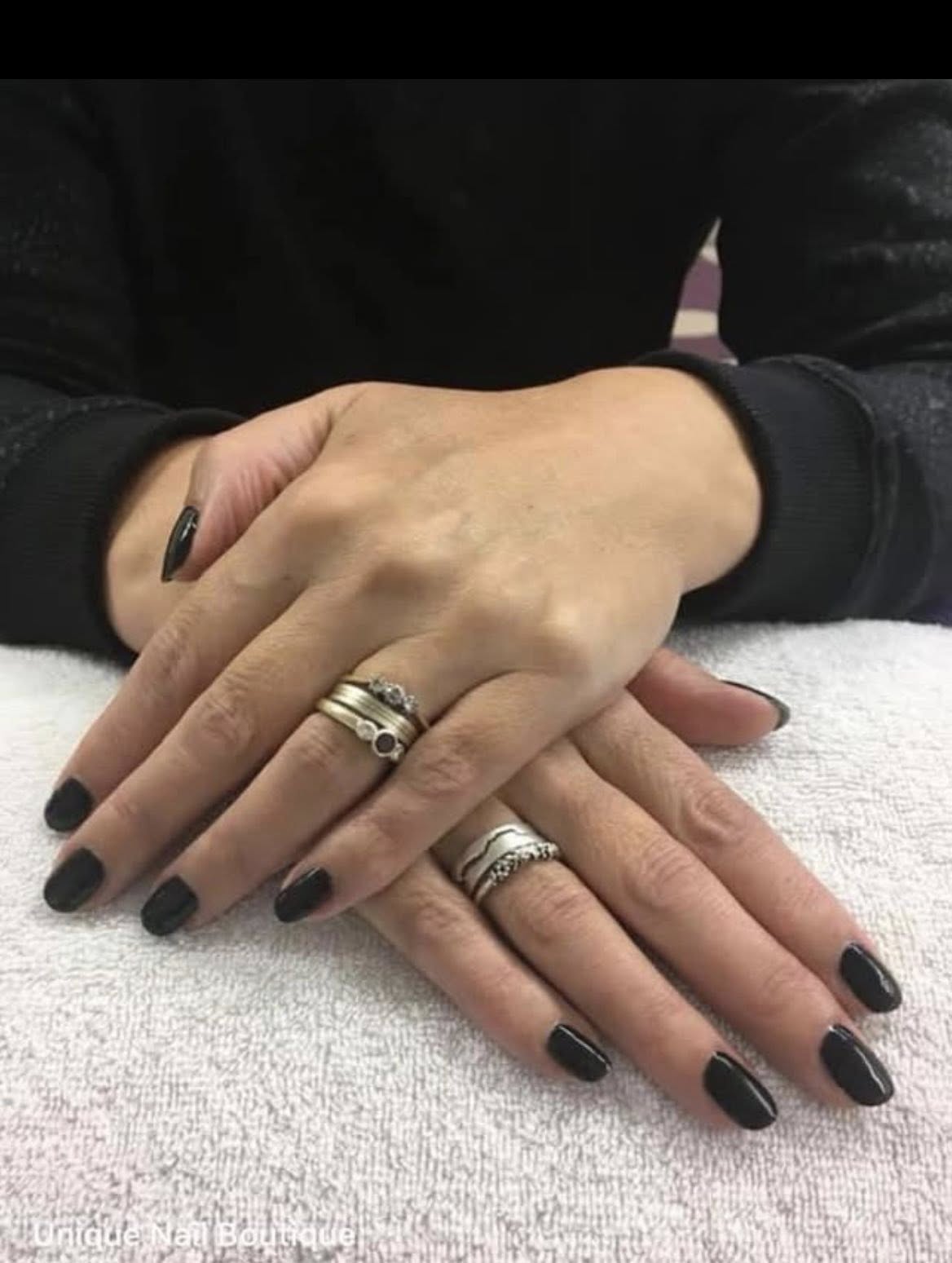 Statement black gel manicure on hands resting on a white towel.
